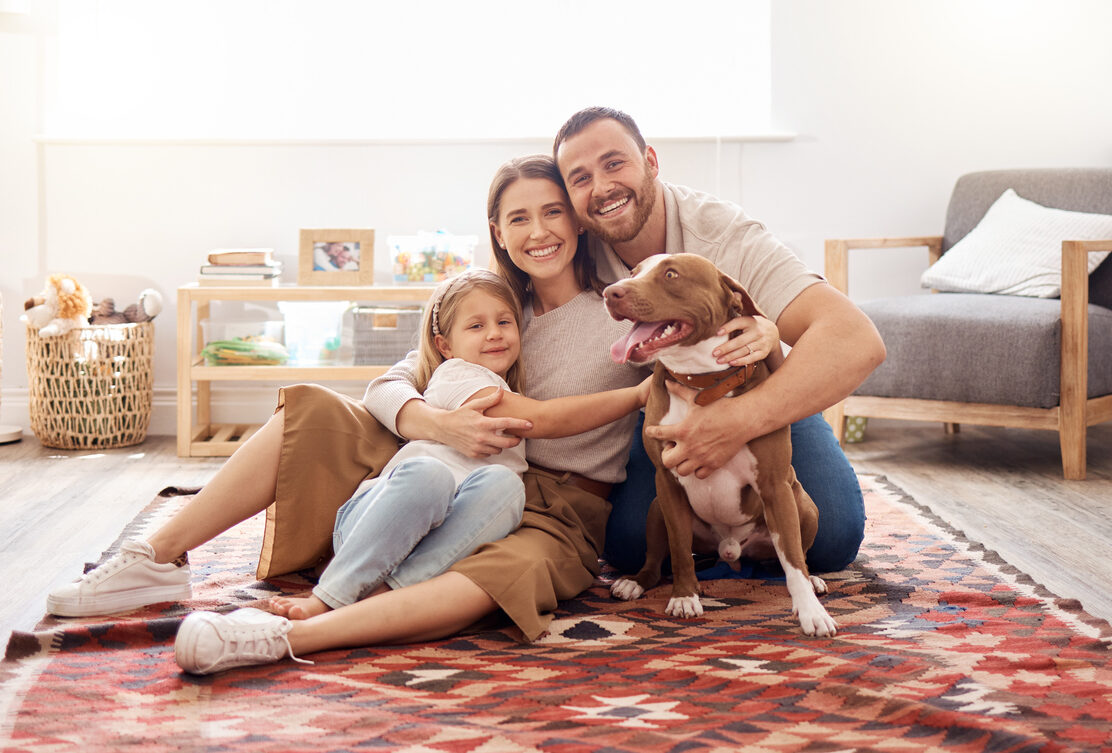 Full Length Shot Of A Young Family Sitting With Their Dog On The Living Room Floor At Home
