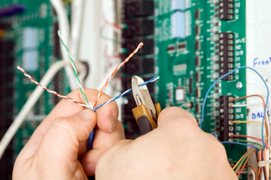 Electrician Cutting Small Paired Wire With Blurred PC Board Background